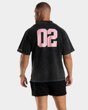 [men] Man wearing an EVDNCE 02 washed black t-shirt with pink numbers on the back against a white background