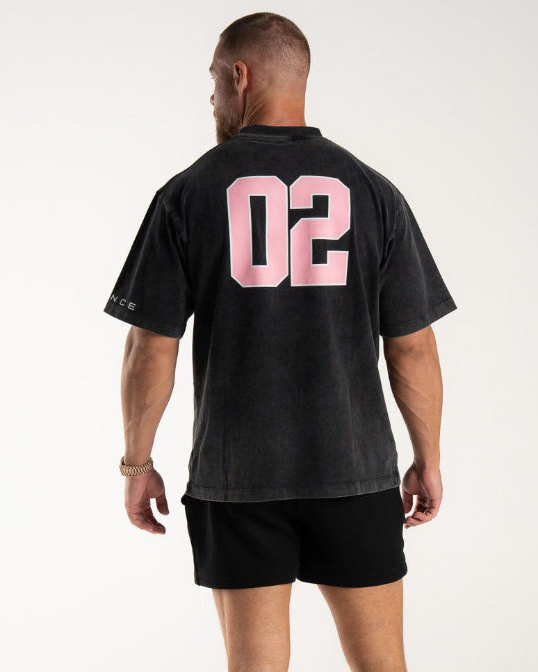 Man wearing an EVDNCE 02 washed black t-shirt with pink numbers on the back against a white background