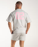 Person wearing a grey Marl EVDNCE 02 t-shirt with pink numbers on the back against a white background